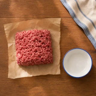 Raw ground beef portion on butcher paper beside small bowl on wood counter
